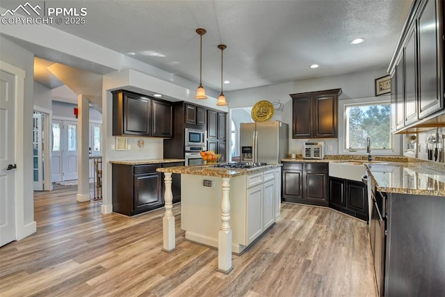 kitchen featuring a kitchen island, stainless steel appliances, decorative light fixtures, and light hardwood / wood-style floors