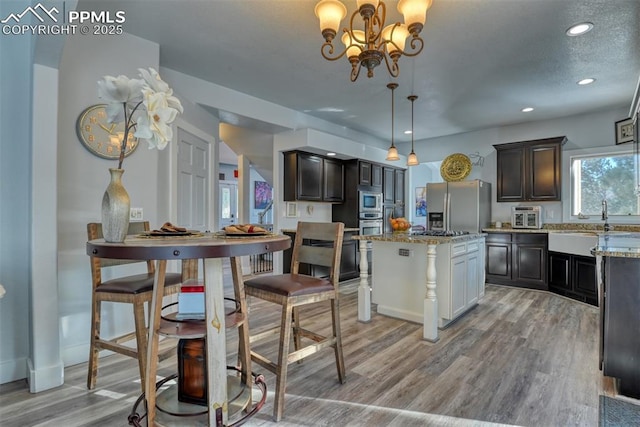 kitchen with appliances with stainless steel finishes, pendant lighting, light hardwood / wood-style flooring, a notable chandelier, and a center island