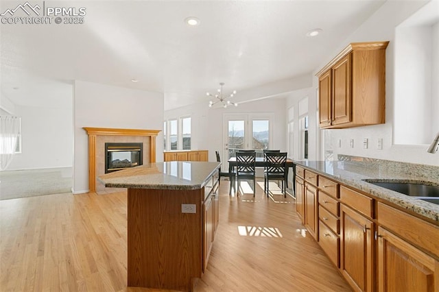 kitchen with a center island, light stone counters, a fireplace, sink, and an inviting chandelier