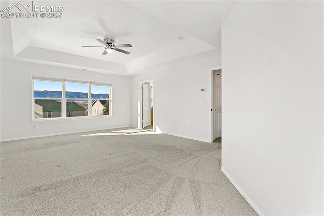 unfurnished room with a raised ceiling, light colored carpet, ceiling fan, and a mountain view