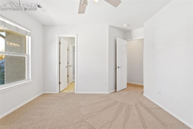 unfurnished bedroom featuring ceiling fan, light colored carpet, ensuite bathroom, and multiple windows