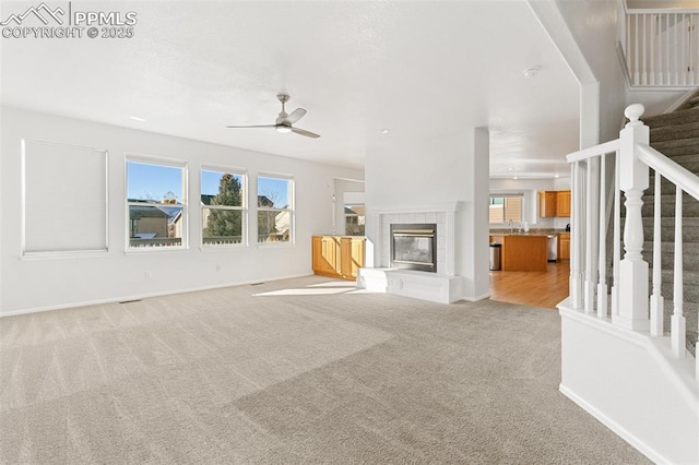 unfurnished living room with a fireplace, ceiling fan, and light colored carpet