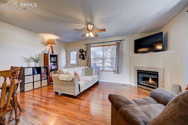 living room with hardwood / wood-style floors, ceiling fan, and a tile fireplace