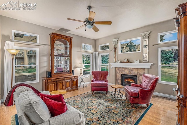 living room featuring a tiled fireplace, ceiling fan, and light hardwood / wood-style flooring