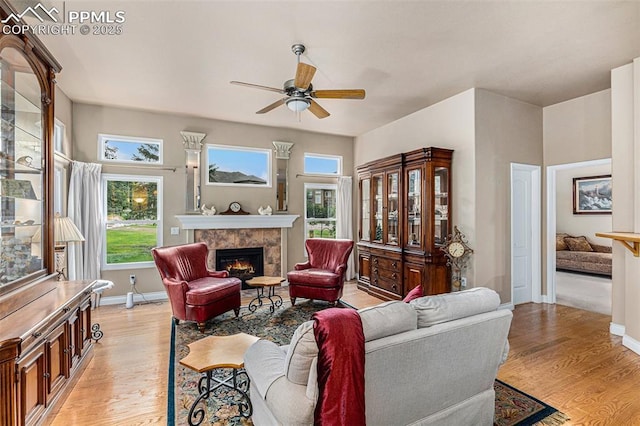 living room with a tile fireplace, ceiling fan, and light hardwood / wood-style flooring