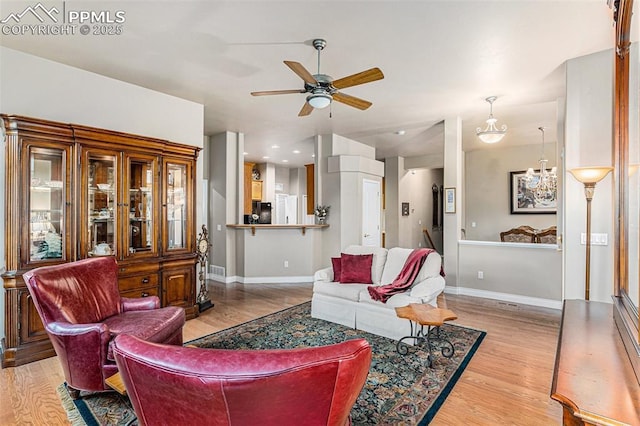 living room with light wood-type flooring and ceiling fan with notable chandelier