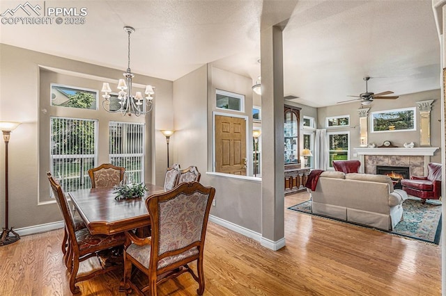 dining space with ceiling fan with notable chandelier, light hardwood / wood-style flooring, and a fireplace