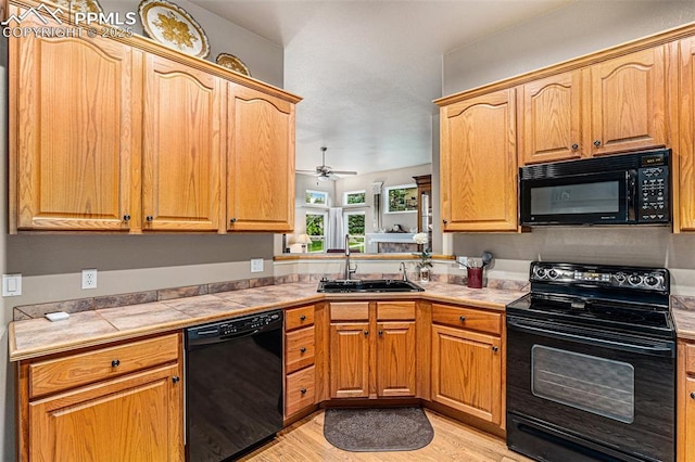 kitchen featuring tile countertops, black appliances, light wood-type flooring, ceiling fan, and sink