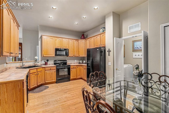 kitchen featuring black appliances, light wood-type flooring, washing machine and dryer, tile countertops, and sink