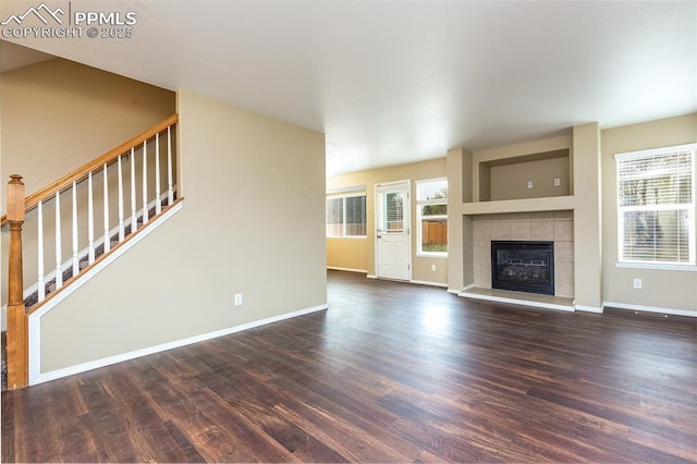 unfurnished living room featuring a tiled fireplace, dark wood-type flooring, and a healthy amount of sunlight