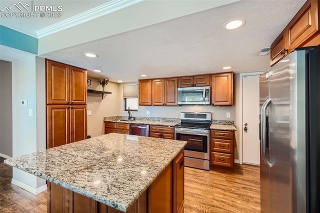 kitchen featuring light stone countertops, light wood-type flooring, stainless steel appliances, crown molding, and a center island