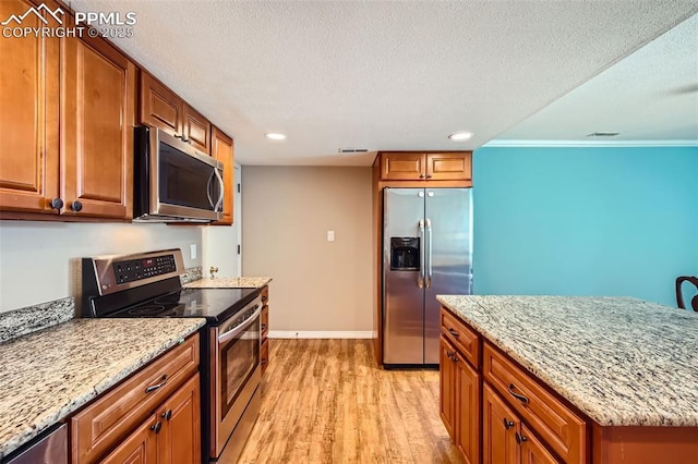 kitchen featuring light stone countertops, a textured ceiling, stainless steel appliances, and light hardwood / wood-style flooring