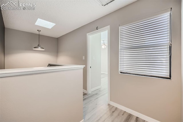 corridor featuring light hardwood / wood-style floors, a textured ceiling, and a skylight