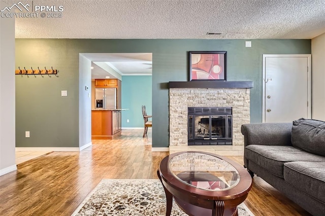 living room featuring a fireplace, a textured ceiling, light hardwood / wood-style flooring, and crown molding