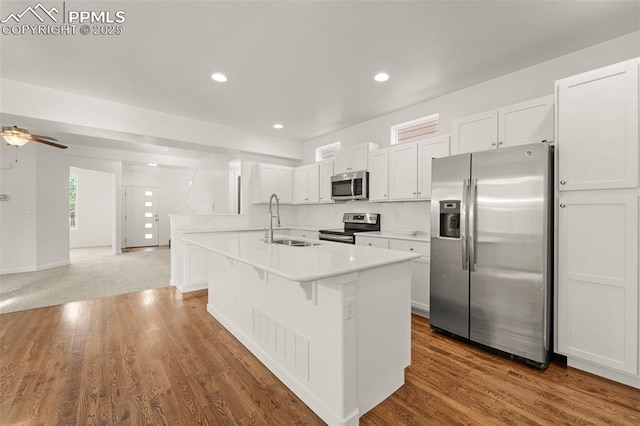 kitchen with appliances with stainless steel finishes, ceiling fan, sink, white cabinetry, and an island with sink