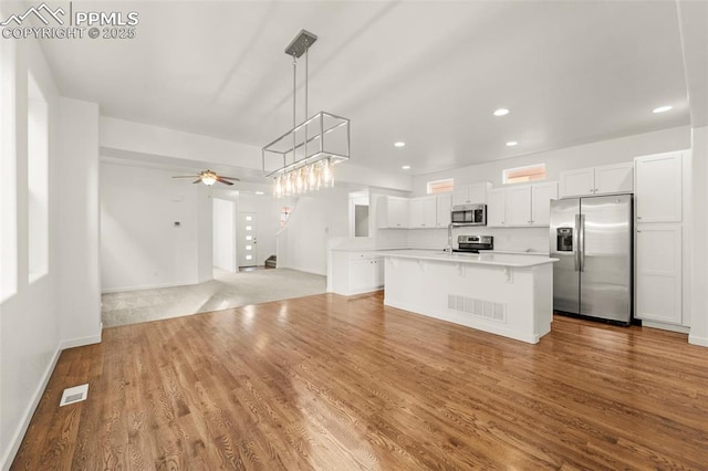 kitchen with stainless steel appliances, a kitchen island, ceiling fan, pendant lighting, and white cabinetry