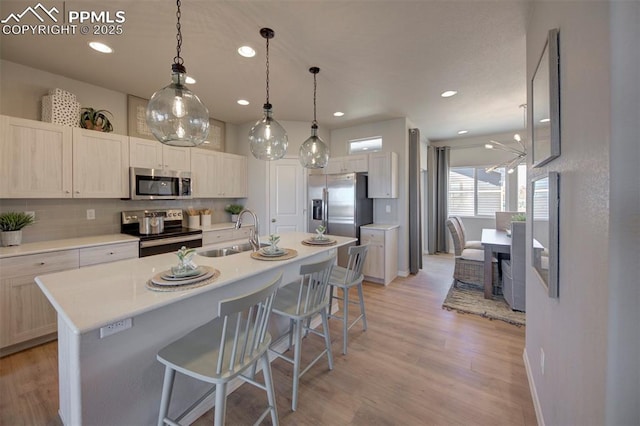 kitchen featuring appliances with stainless steel finishes, backsplash, sink, light hardwood / wood-style floors, and an island with sink