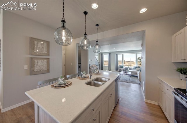 kitchen with dishwasher, sink, light hardwood / wood-style flooring, pendant lighting, and a center island with sink