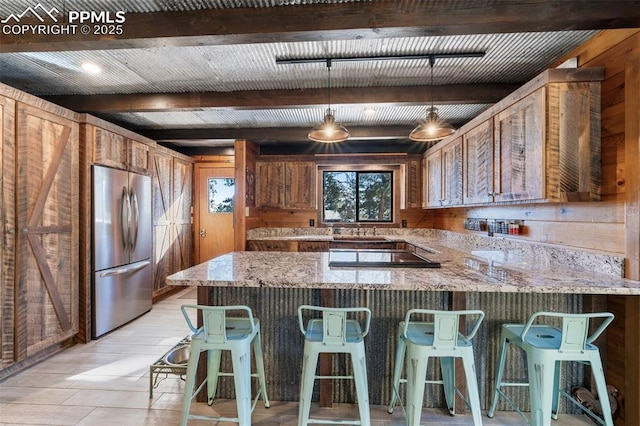 kitchen with a breakfast bar, pendant lighting, stainless steel fridge, black electric stovetop, and light stone countertops