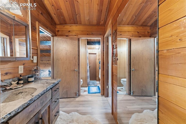 bathroom with toilet, wood-type flooring, wooden ceiling, vanity, and wooden walls