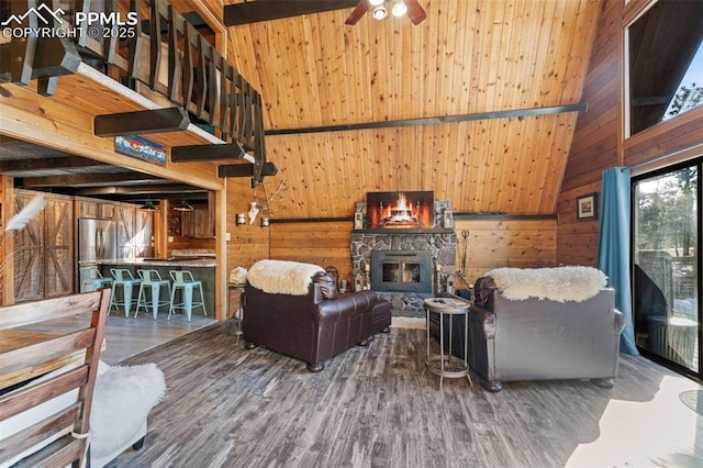 living room featuring hardwood / wood-style flooring, a towering ceiling, a stone fireplace, and wood walls