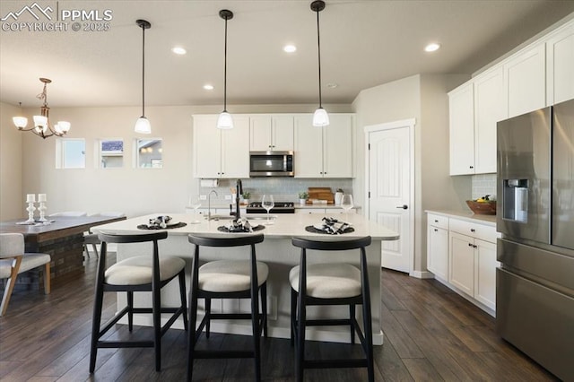 kitchen featuring hanging light fixtures, dark hardwood / wood-style flooring, a kitchen island with sink, white cabinets, and appliances with stainless steel finishes