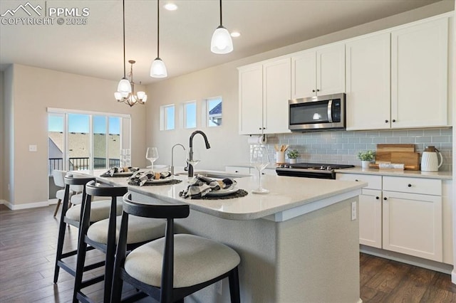 kitchen with white cabinetry, hanging light fixtures, backsplash, a kitchen island with sink, and range