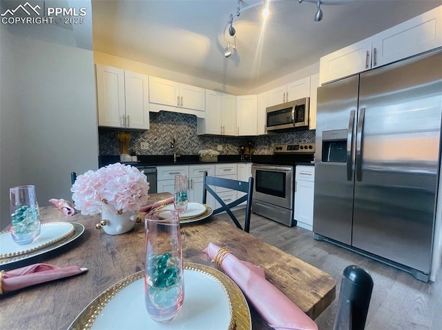 kitchen with white cabinets, sink, light wood-type flooring, appliances with stainless steel finishes, and tasteful backsplash