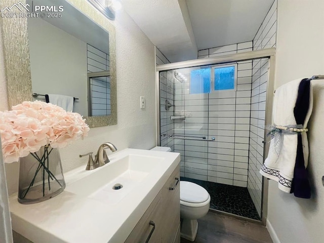 bathroom with wood-type flooring, vanity, toilet, and a shower with shower door