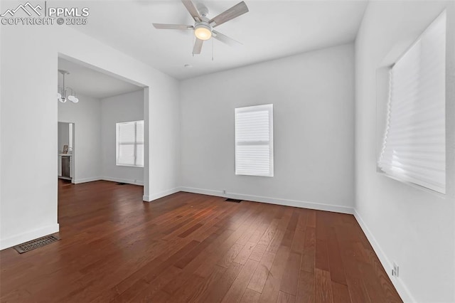 empty room with ceiling fan with notable chandelier and dark wood-type flooring