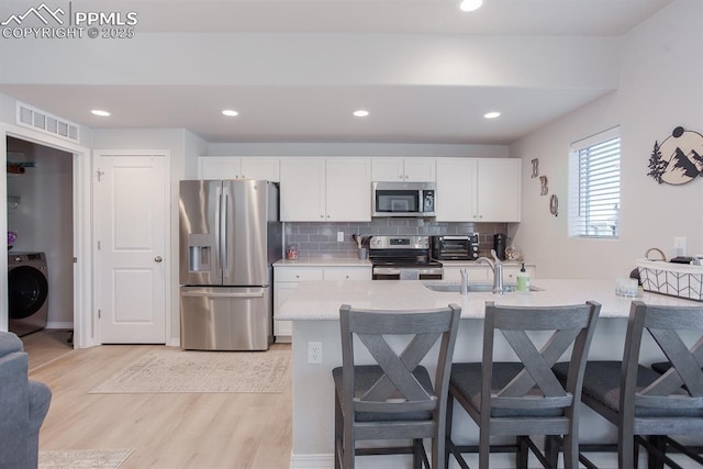 kitchen with light hardwood / wood-style flooring, backsplash, washer / clothes dryer, white cabinets, and appliances with stainless steel finishes