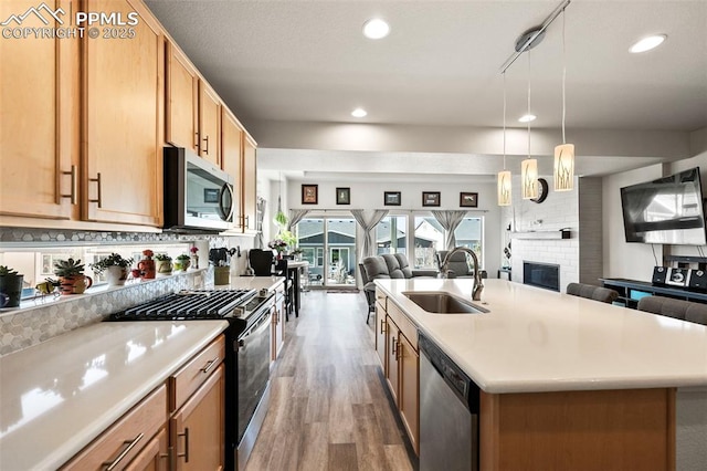 kitchen with a center island with sink, appliances with stainless steel finishes, sink, decorative light fixtures, and backsplash