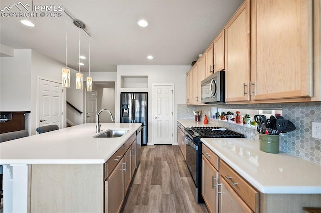 kitchen with stainless steel appliances, a center island with sink, and light brown cabinetry