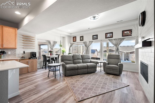 living room featuring a tile fireplace, light wood-type flooring, a raised ceiling, and a wealth of natural light