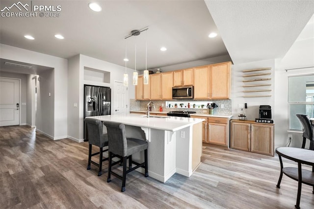 kitchen featuring a kitchen island with sink, hanging light fixtures, sink, backsplash, and refrigerator with ice dispenser