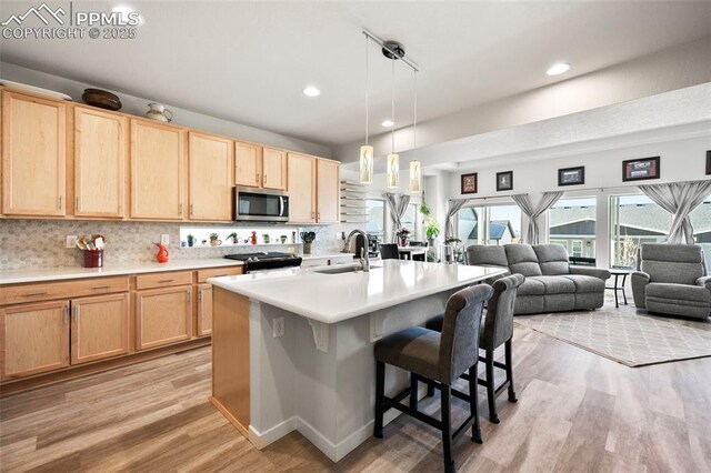 kitchen featuring sink, light hardwood / wood-style flooring, an island with sink, a breakfast bar area, and pendant lighting