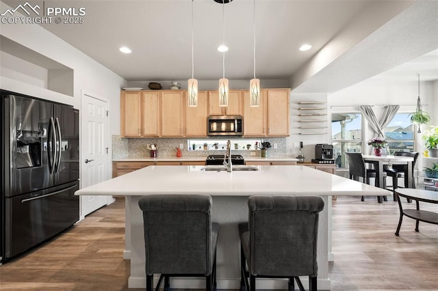 kitchen featuring black refrigerator with ice dispenser, decorative backsplash, a center island with sink, and light brown cabinets