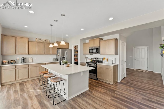 kitchen featuring decorative light fixtures, wood-type flooring, light brown cabinetry, a kitchen island with sink, and appliances with stainless steel finishes