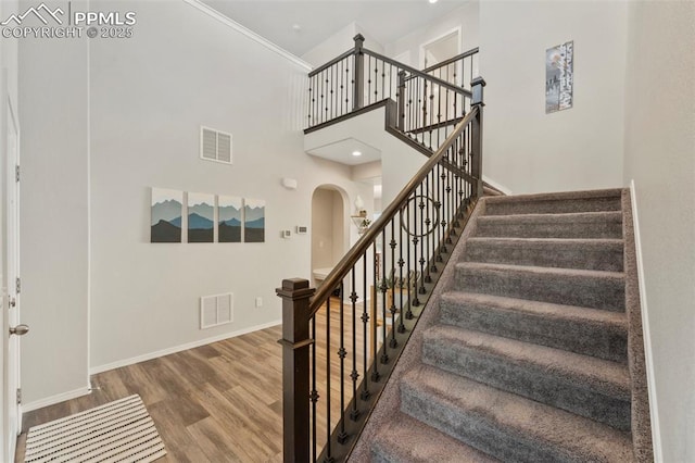 staircase with a high ceiling, hardwood / wood-style flooring, and crown molding