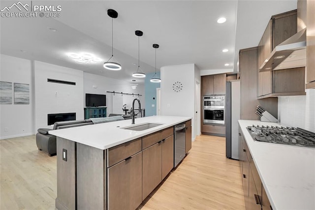 kitchen featuring appliances with stainless steel finishes, light wood-type flooring, backsplash, sink, and a center island with sink