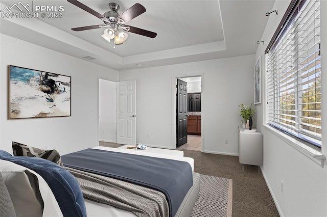 carpeted bedroom featuring ceiling fan, ensuite bathroom, and a tray ceiling