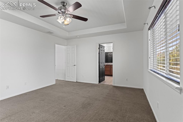 unfurnished bedroom with ensuite bathroom, light colored carpet, ceiling fan, and a tray ceiling