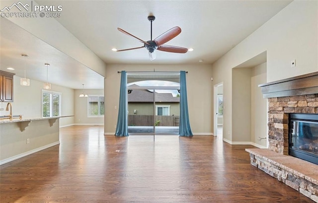 unfurnished living room with a stone fireplace, ceiling fan, dark wood-type flooring, and sink