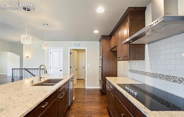 kitchen featuring pendant lighting, black electric stovetop, wall chimney range hood, sink, and light stone counters