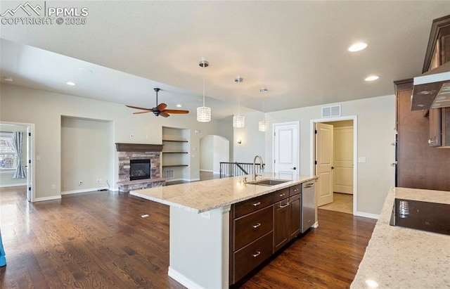 kitchen featuring dark brown cabinetry, sink, decorative light fixtures, built in features, and a center island with sink