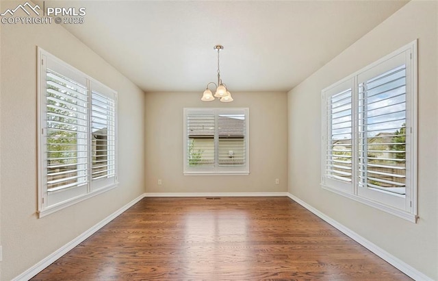 empty room featuring a chandelier, dark wood-type flooring, and a healthy amount of sunlight