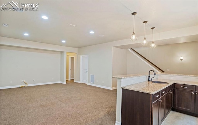 kitchen featuring sink, light stone counters, decorative light fixtures, light carpet, and dark brown cabinets