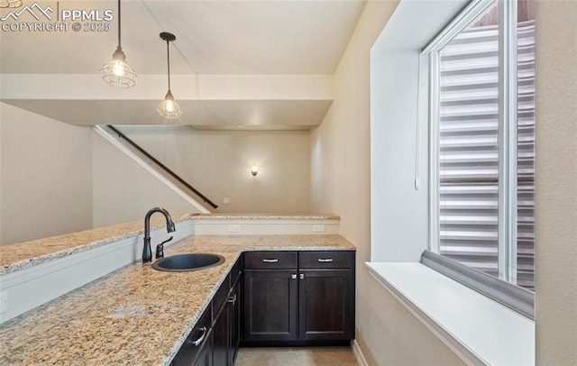 kitchen with decorative light fixtures, light stone counters, and sink