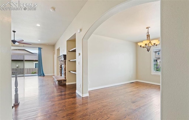 empty room with ceiling fan with notable chandelier, built in features, and dark wood-type flooring