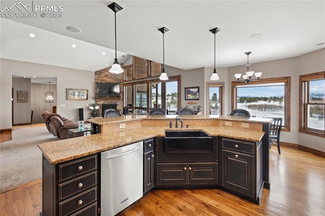 kitchen featuring a center island with sink, dishwasher, light stone counters, and hanging light fixtures